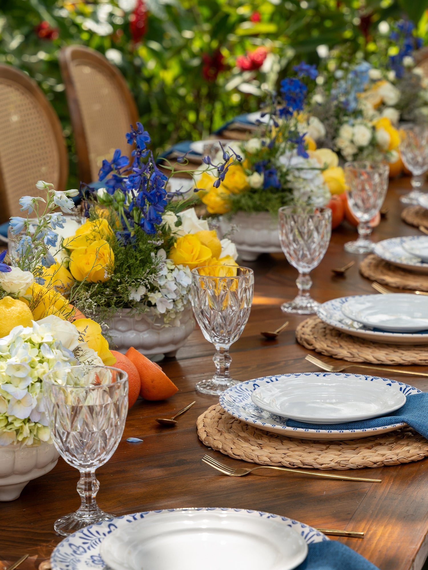 Outdoor spring tablescape with yellow, blue, and white floral centerpieces on a dining table