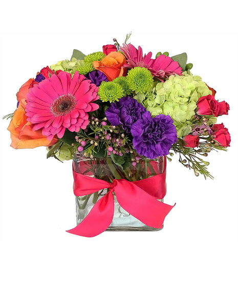 mostly hot pink, purple, orange & green flowers in a glass cube