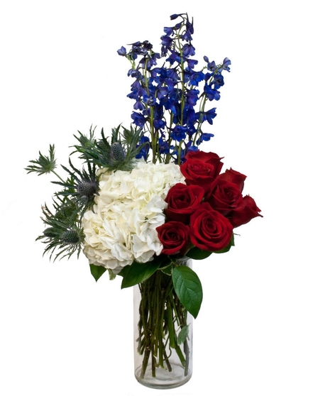 red roses, blue delphinium, and white hydrangea in a cylinder vase